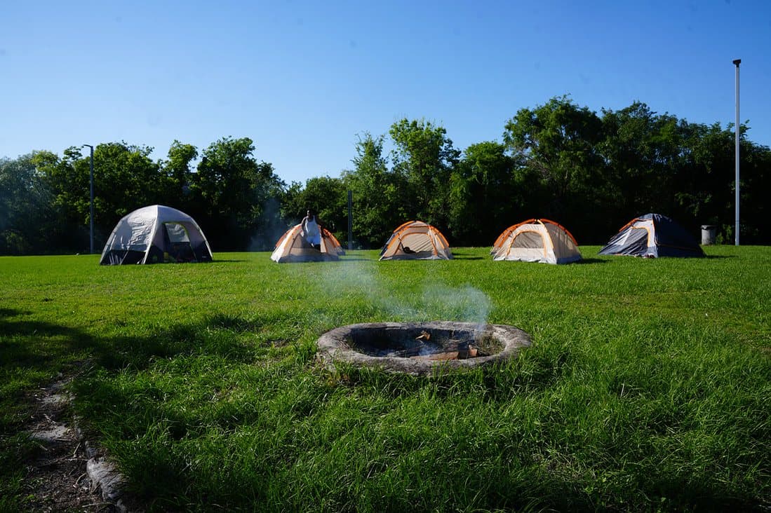 Tents pitched on a green field with a campfire ring